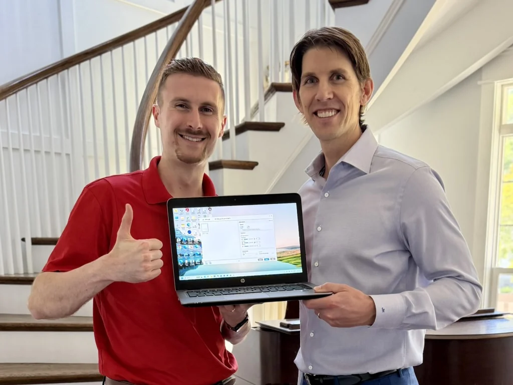Preston and a man holding a laptop together beside a staircase.