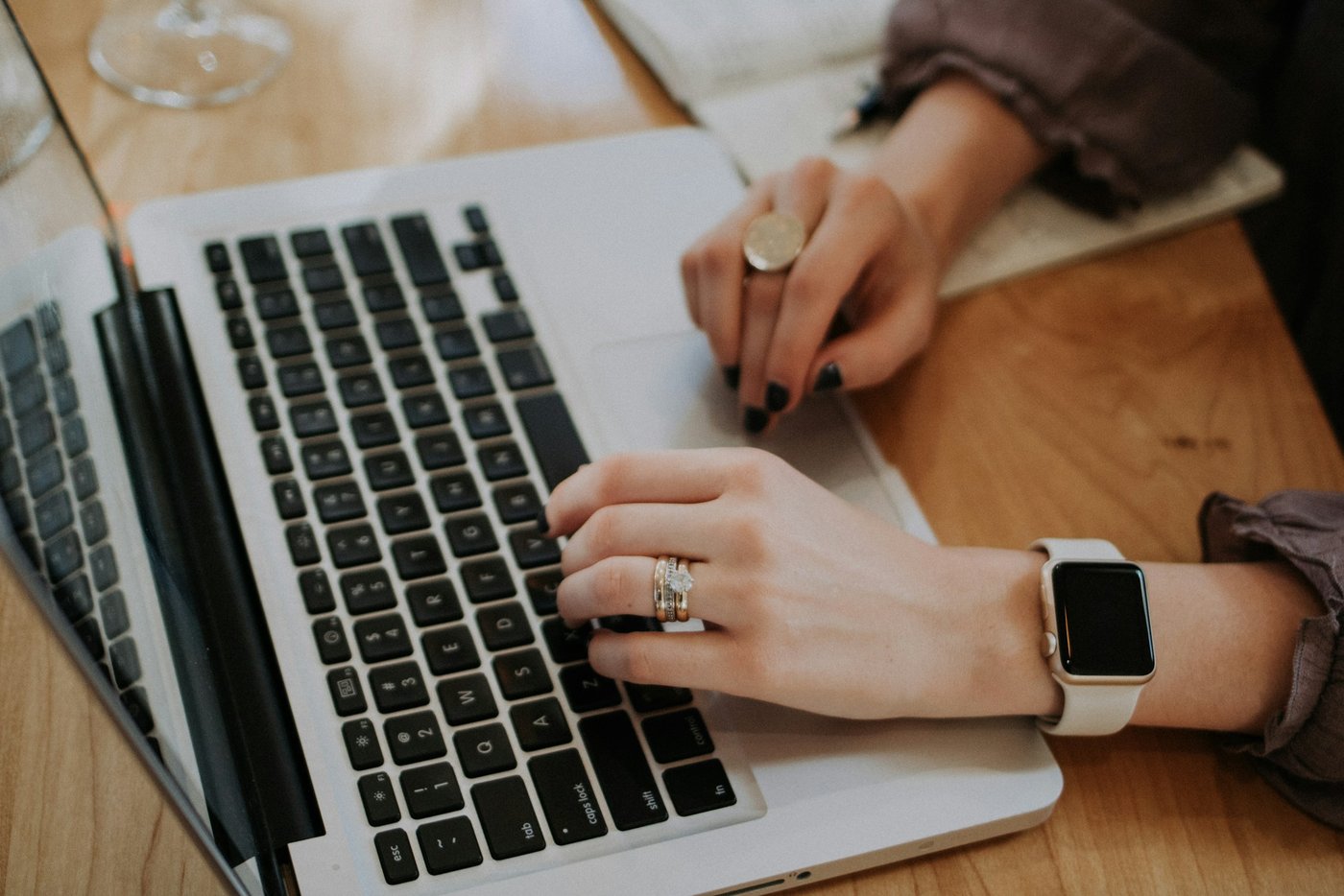 Close-up of hands typing on a laptop at a wooden cafe table